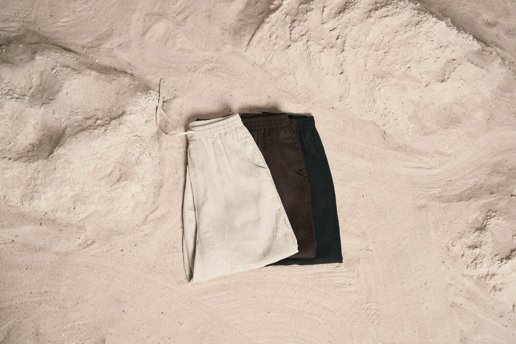 Tre pantaloncini in lino, chiaro, marrone e nero, piegati sulla sabbia